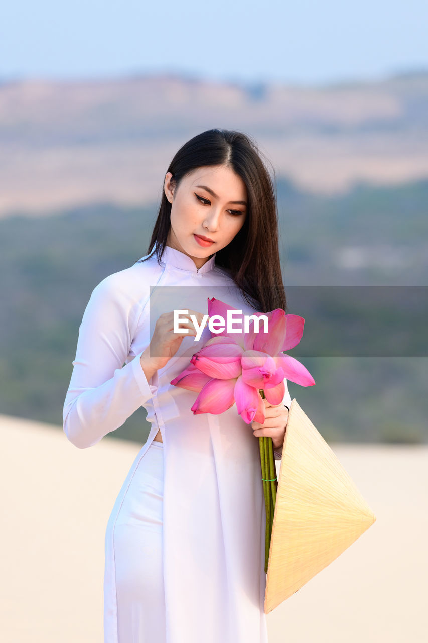 Beautiful young woman holding lotus water lilies while standing in desert