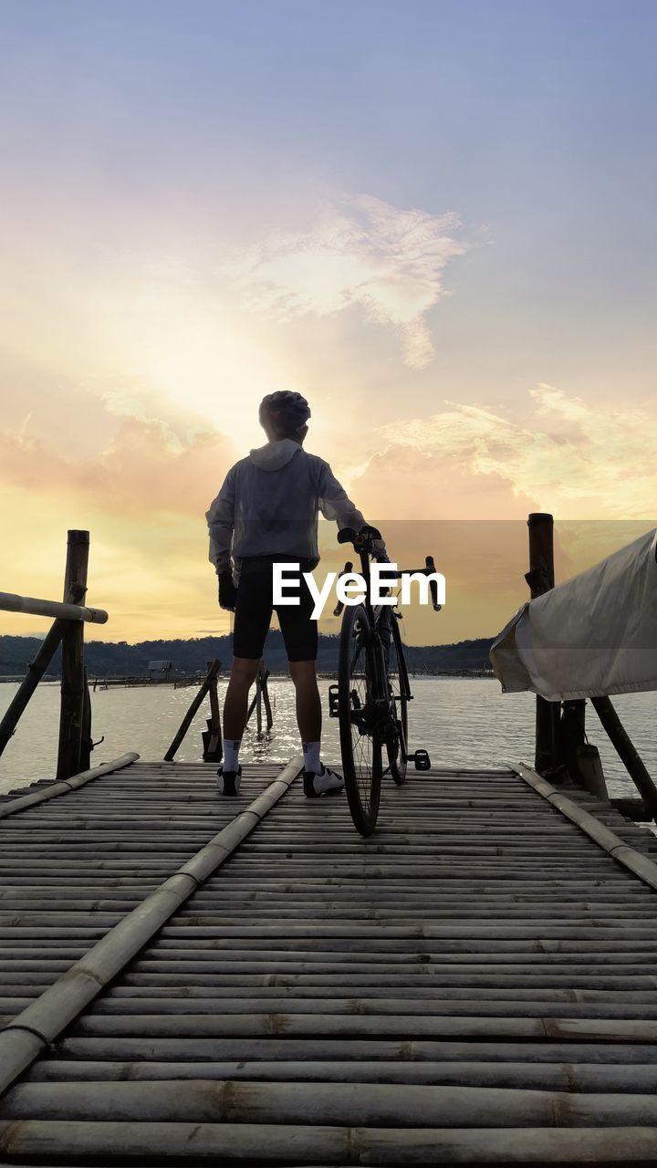 REAR VIEW OF MAN RIDING BICYCLE AGAINST SKY