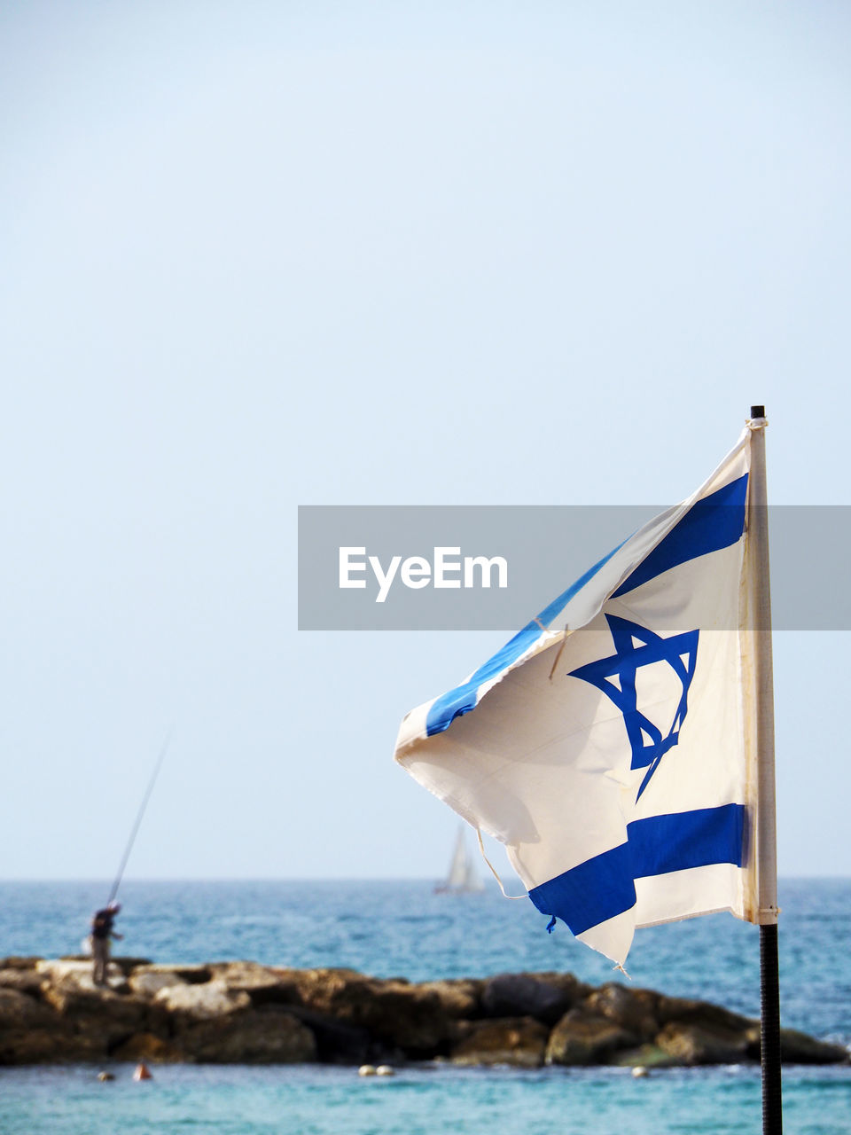 Israeli flag by sea against clear sky
