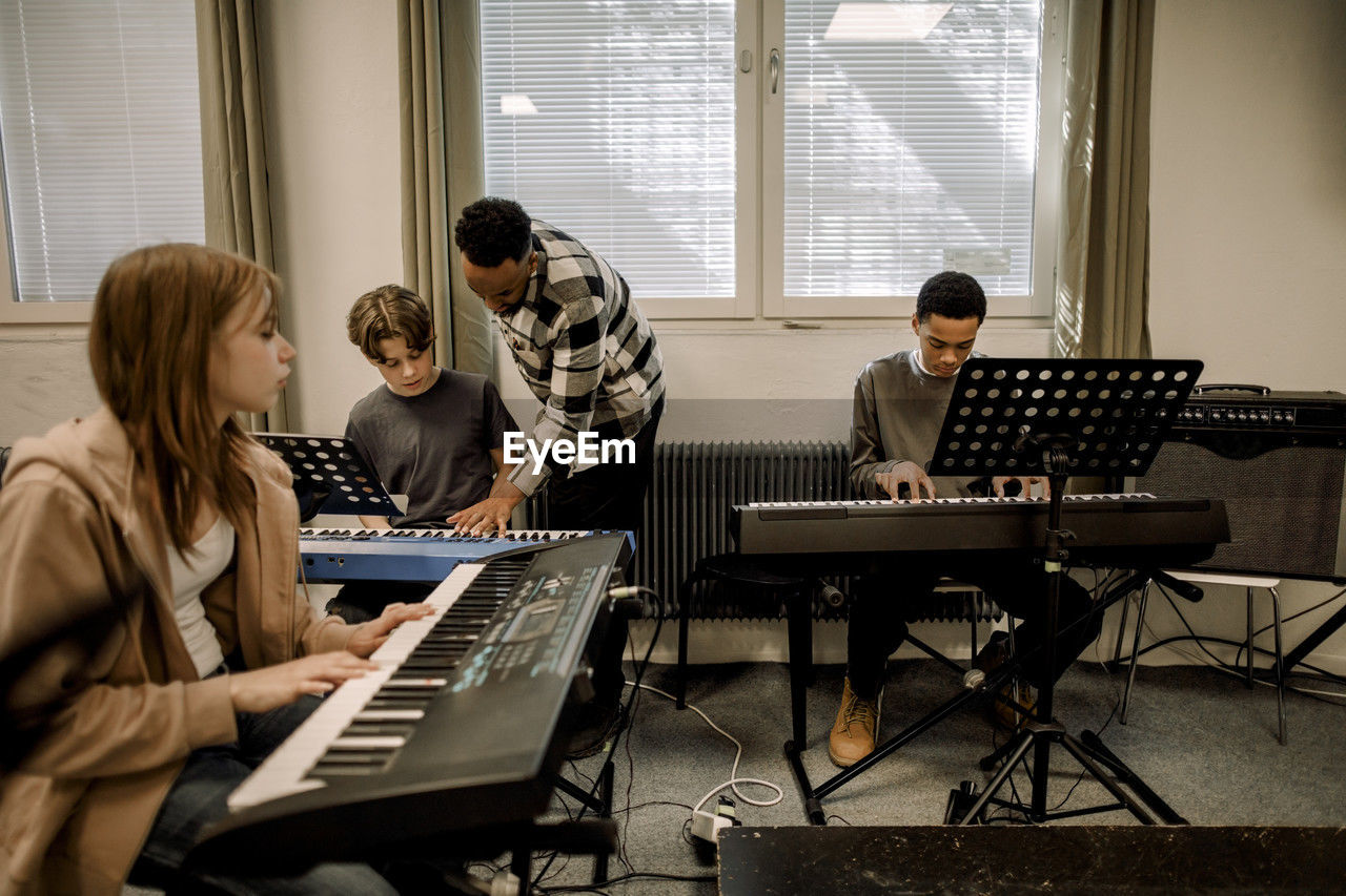 Teacher assisting teenage students during piano class at high school