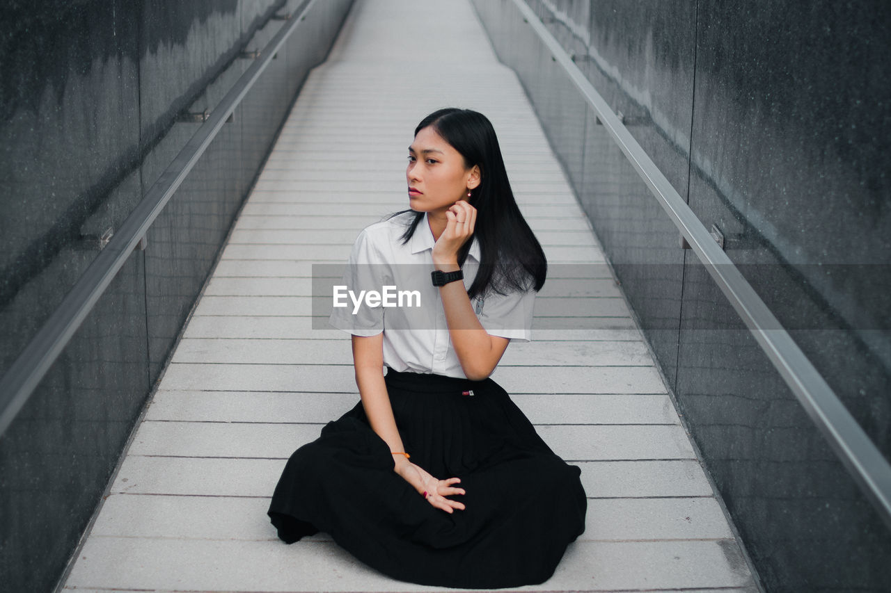 Young woman looking away while sitting on walkway
