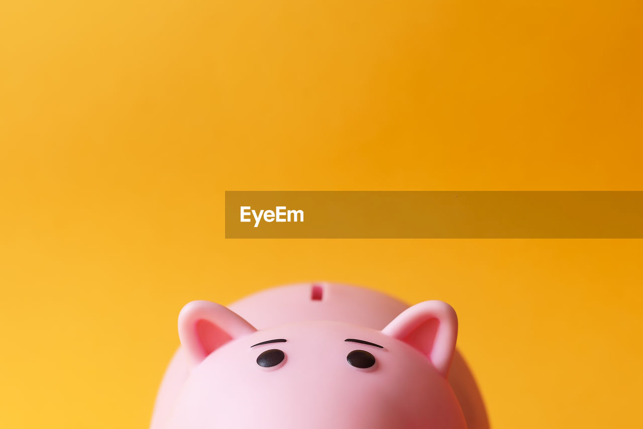 Close-up of pink piggy bank against orange background