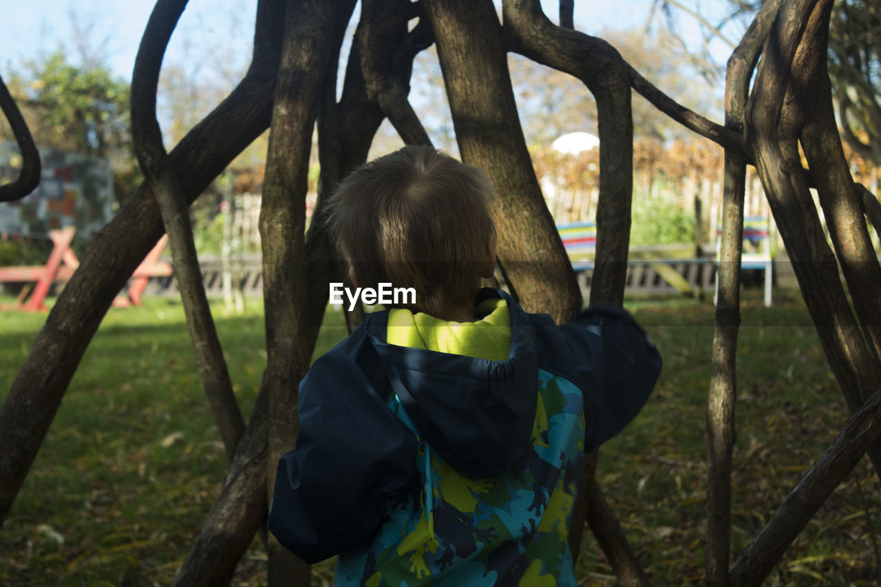 Rear view of boy standing by branches at park