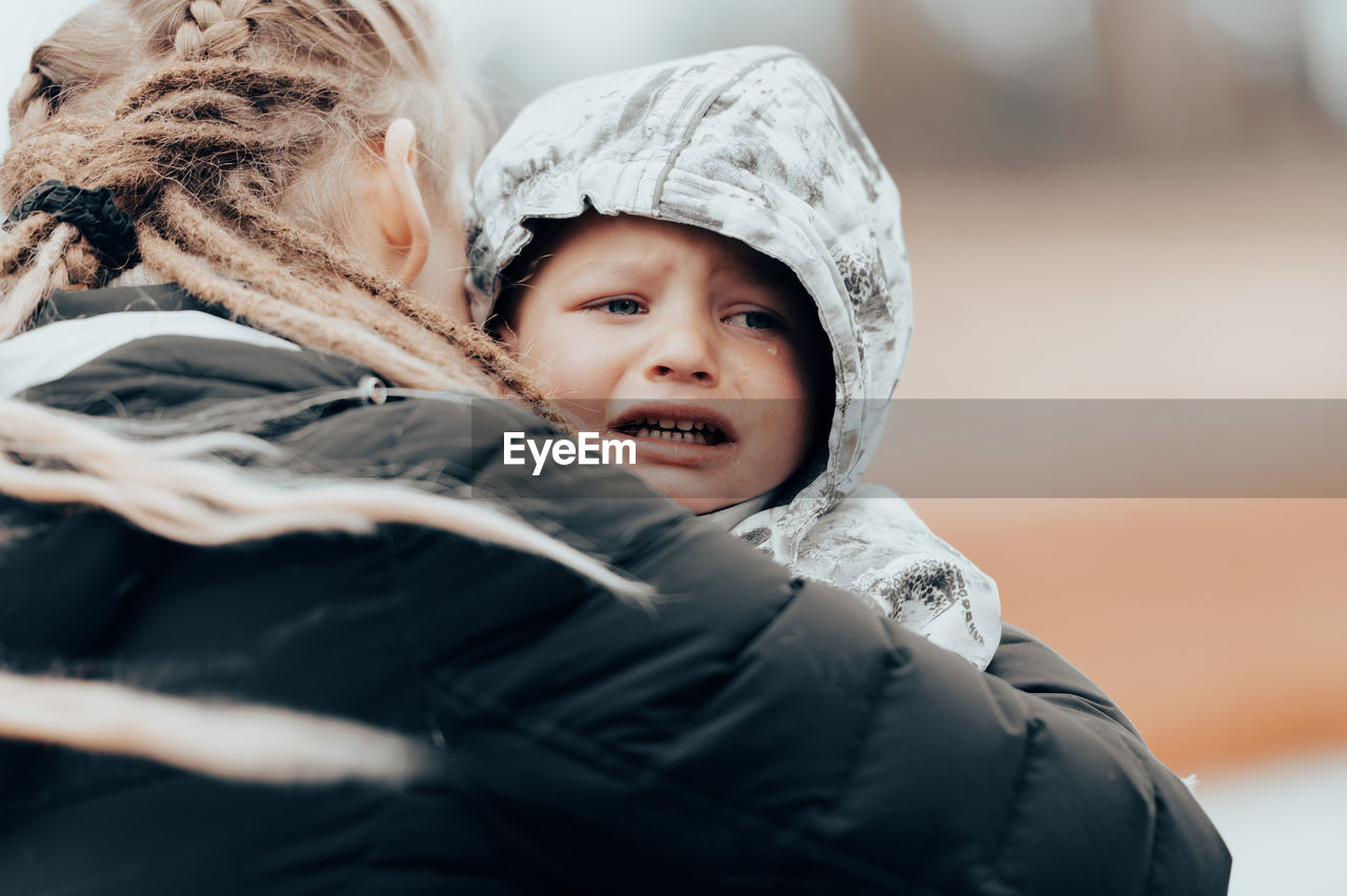 Mother holding crying baby, sad little boy being hugged by his mother