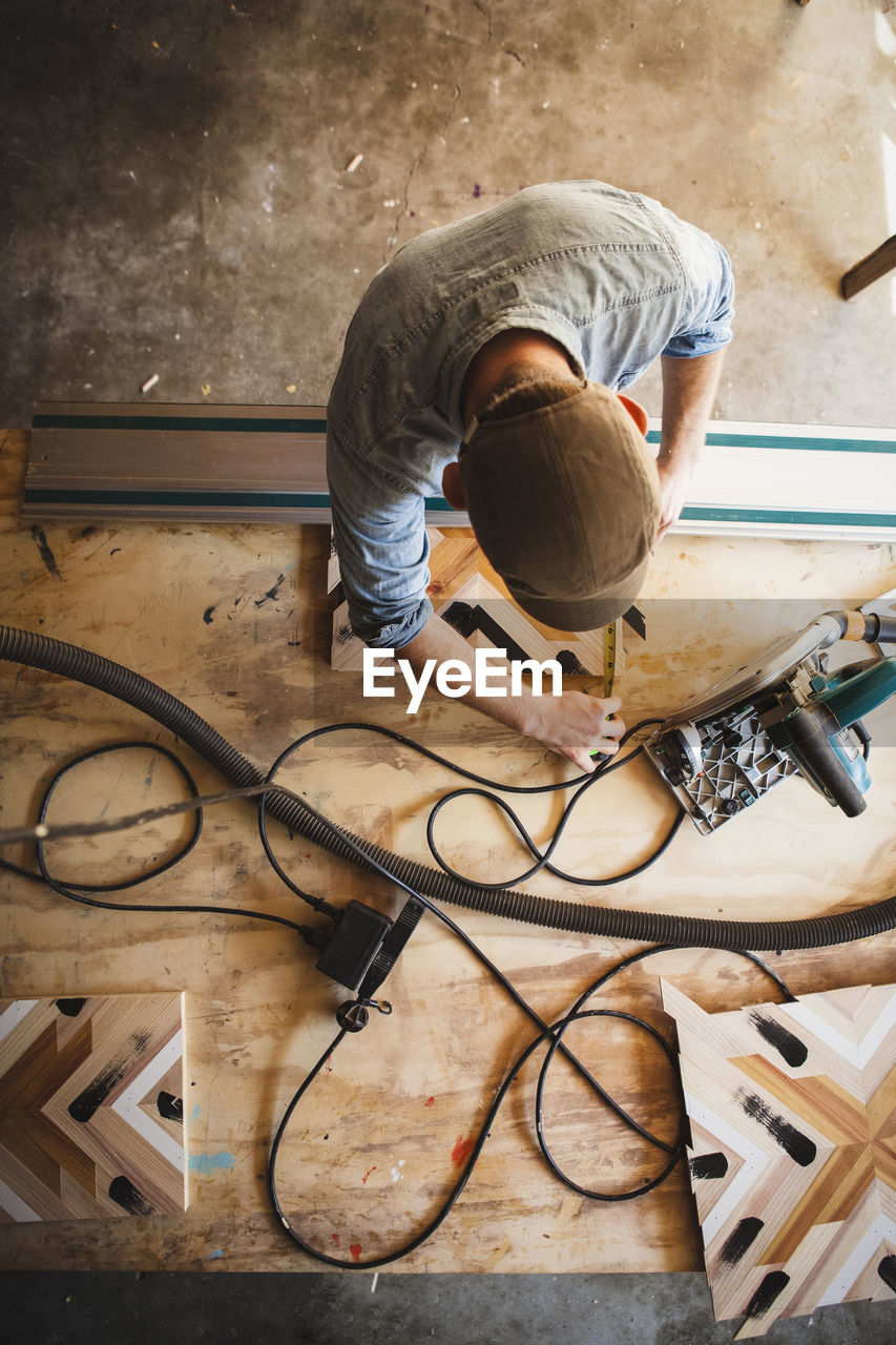 High angle view of craftsperson measuring wooden plank art at workbench