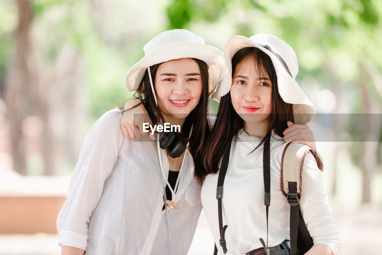 Portrait of smiling young women with arms around against trees