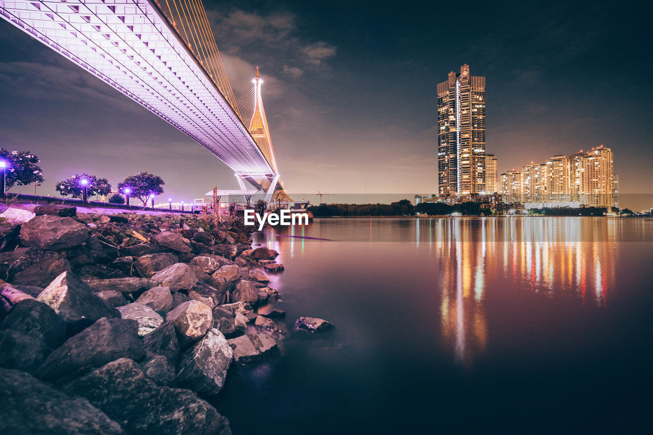 Illuminated bridge over river against sky at night