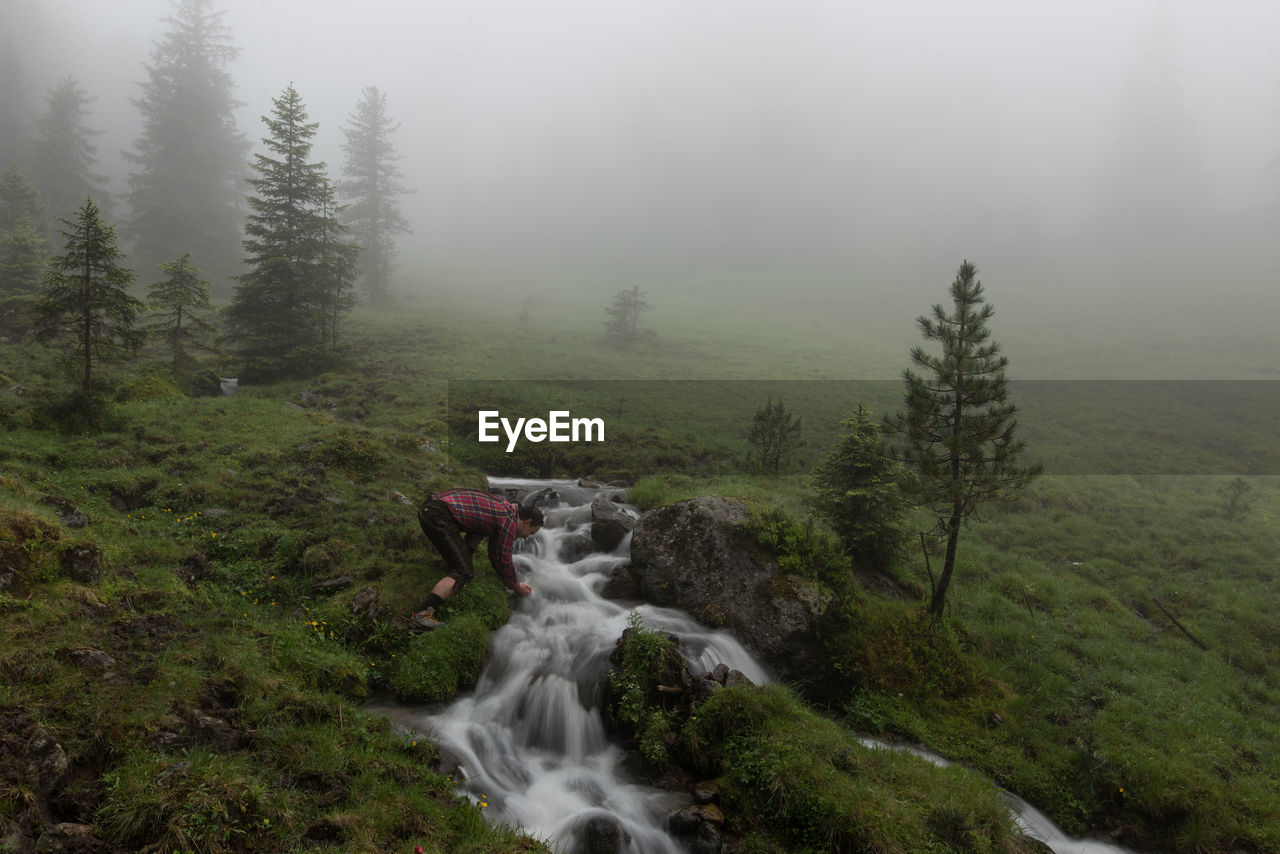 Side view of man bending by stream during foggy weather