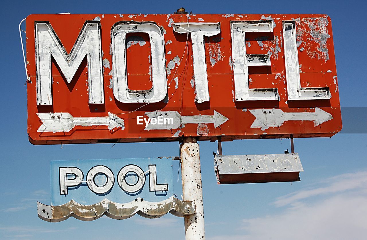 Low angle view of abandoned motel and pool signs against sky