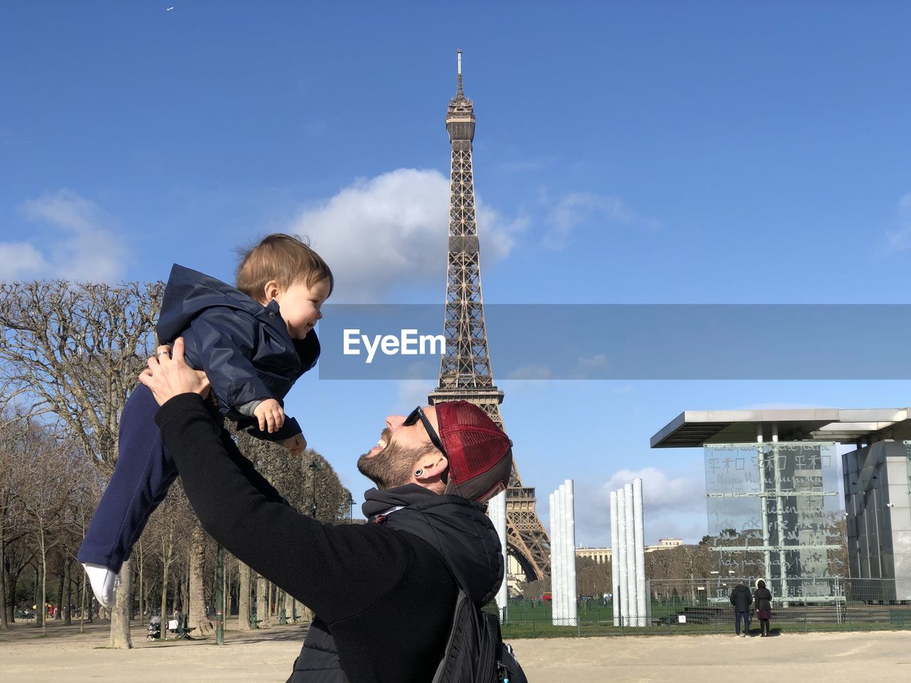 Father catching while playing with son against eiffel tower and sky