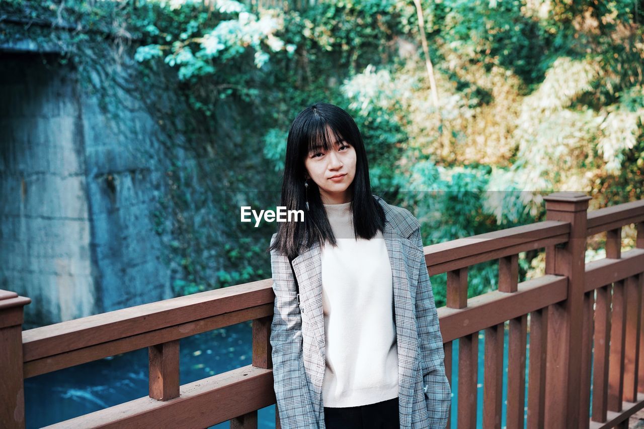 Portrait of young woman standing against railing