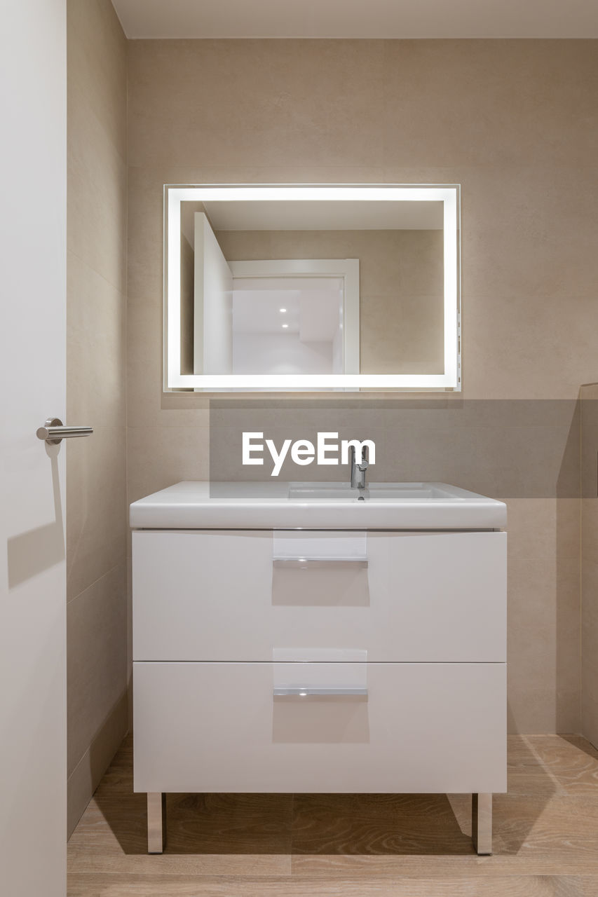 Modern bathroom with beige tiles, furniture and rectangular large mirror with lighting
