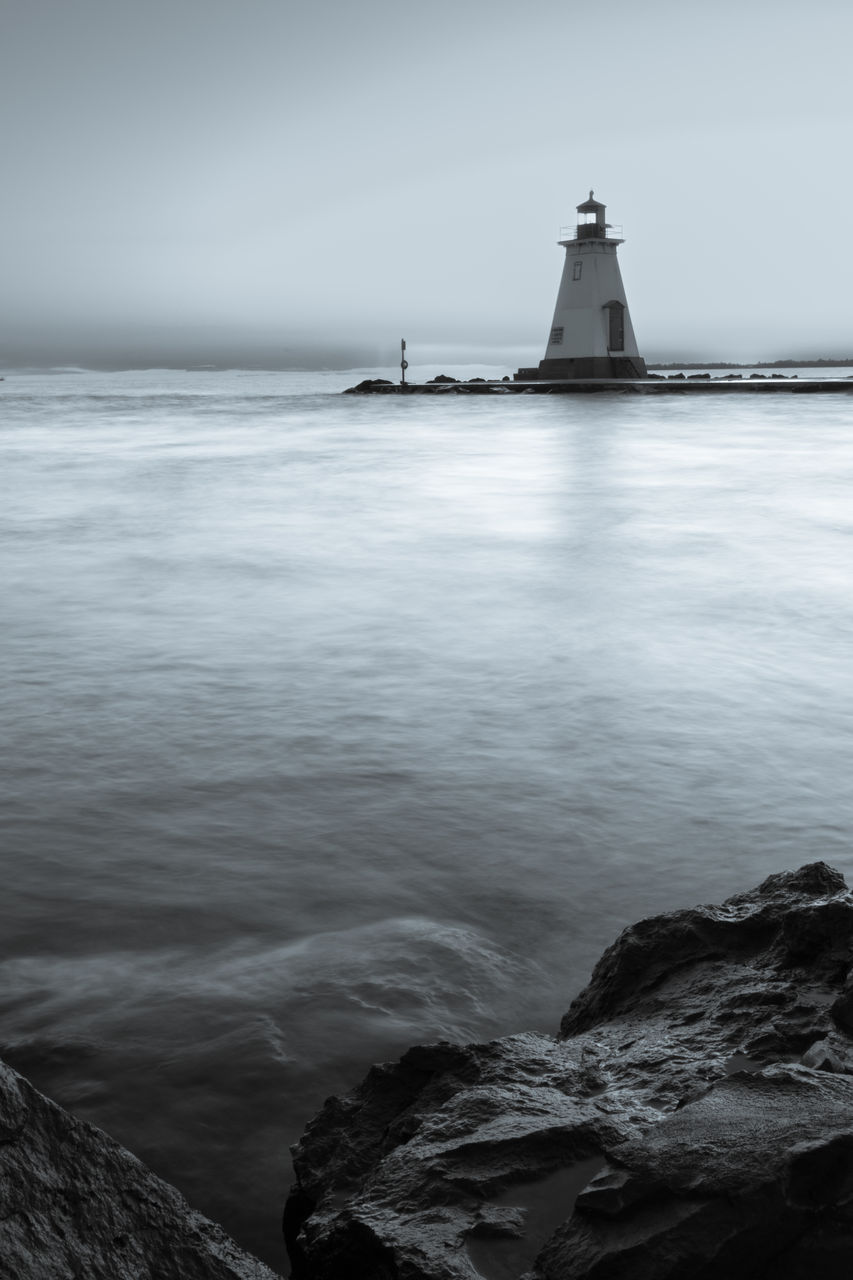 lighthouse, water, sea, tower, guidance, ocean, sky, black and white, architecture, wave, coast, built structure, beach, monochrome, nature, building, monochrome photography, building exterior, land, horizon, scenics - nature, shore, travel destinations, beauty in nature, no people, travel, horizon over water, coastline, rock, tranquility, environment, security, reflection, protection, tranquil scene, nautical vessel, outdoors, landscape, cloud, day, darkness, non-urban scene, breakwater, bay, transportation, tourism, wind wave, seascape, motion, idyllic, water's edge