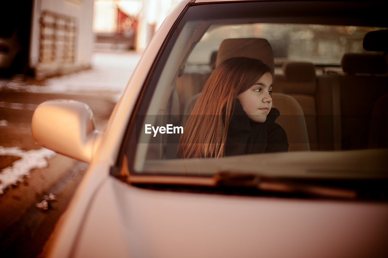 Girl looking away while sitting in car seen through windshield