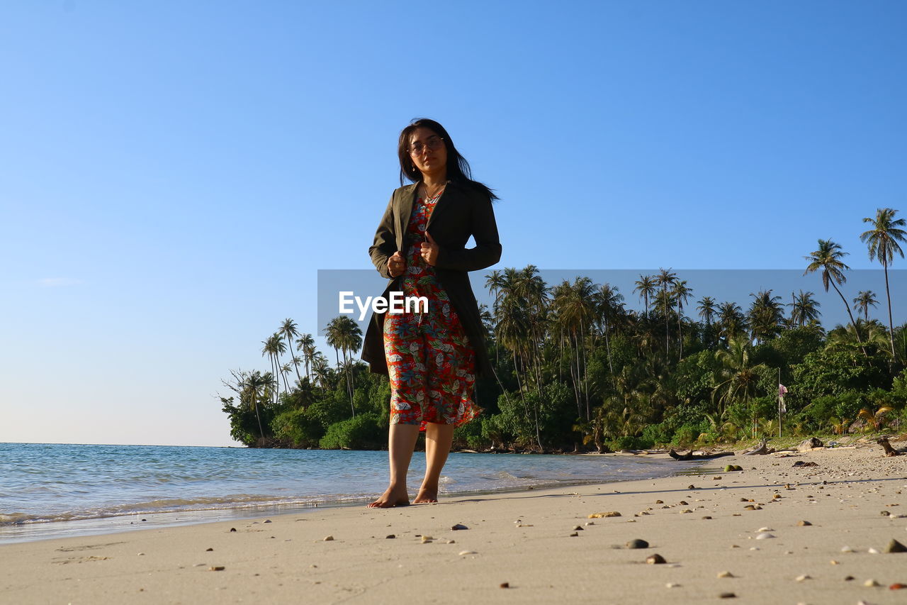 Woman standing at beach against clear blue sky