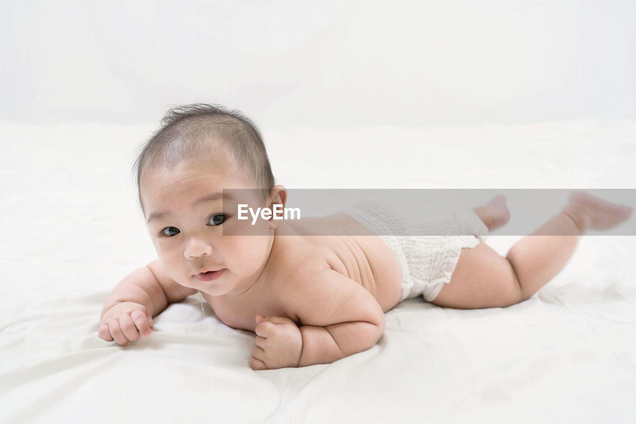 Training tummy time of adorable young asian newborn little baby boy prone on the bed.