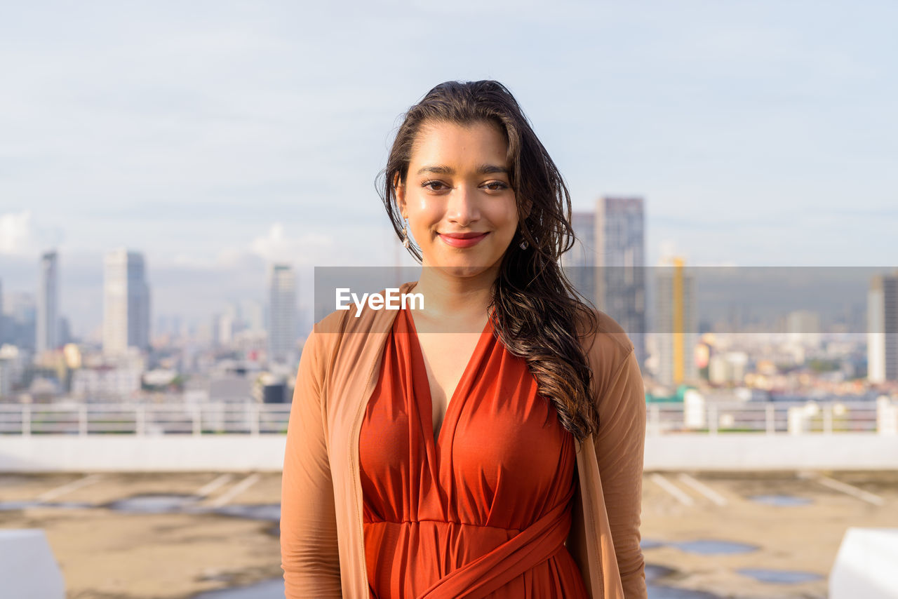 Portrait of smiling young woman standing against cityscape