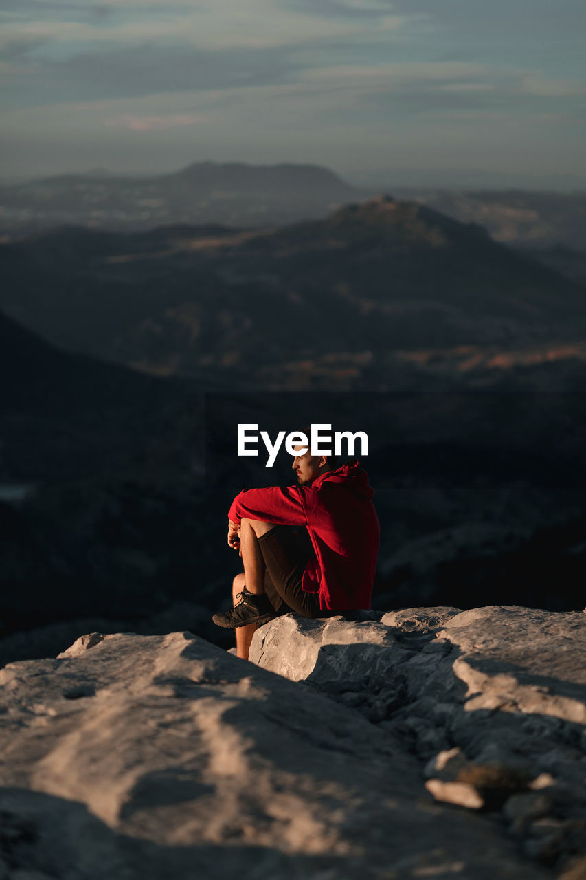 Side view of thoughtful male hiker in casual wear resting on rocky mountain summit and admiring scenic views over rough highlands in seville spain