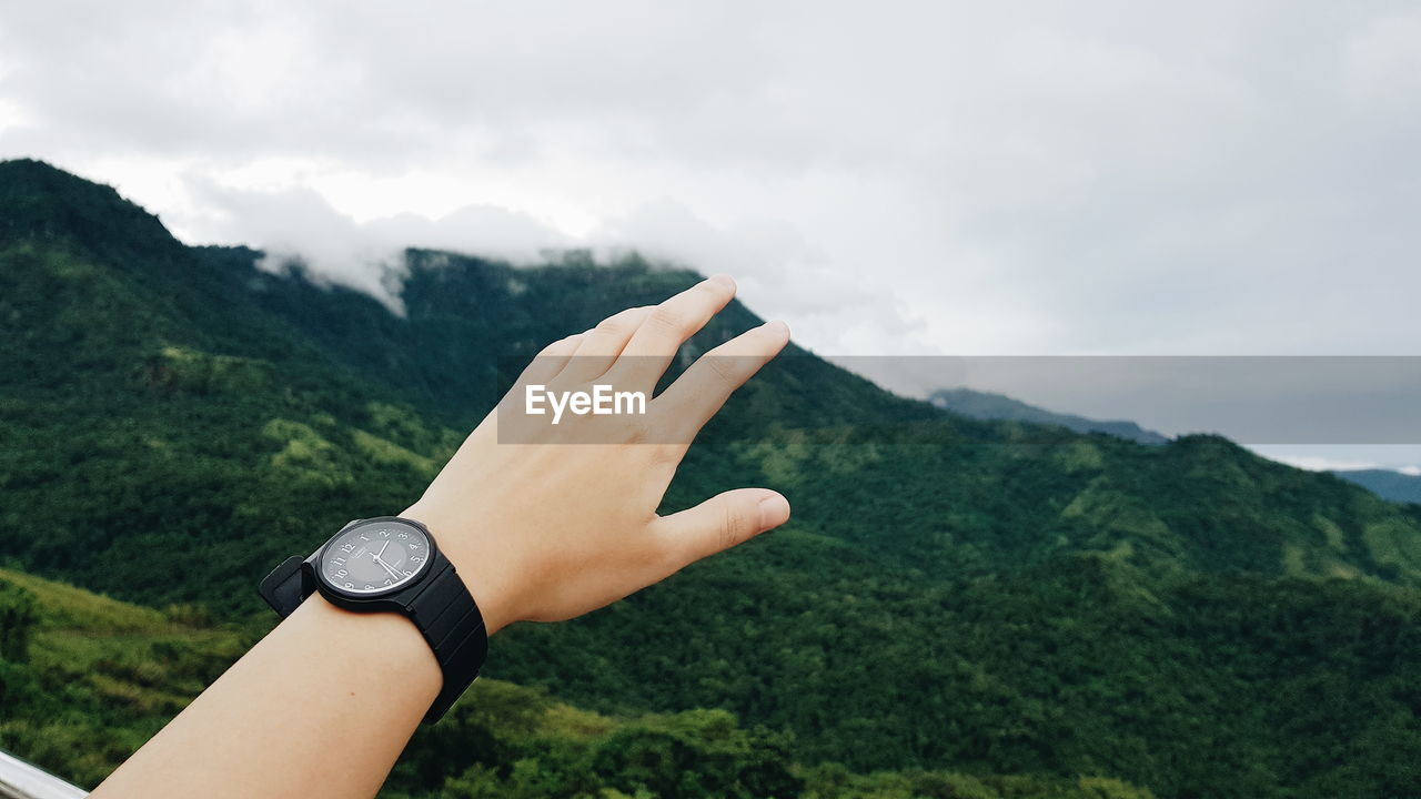 CLOSE-UP OF HAND AGAINST MOUNTAIN