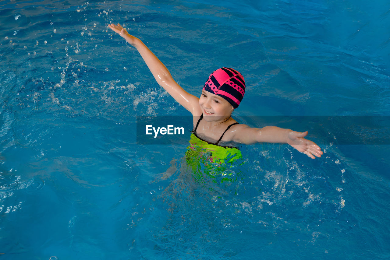 High angle view of girl with arms outstretched swimming in pool