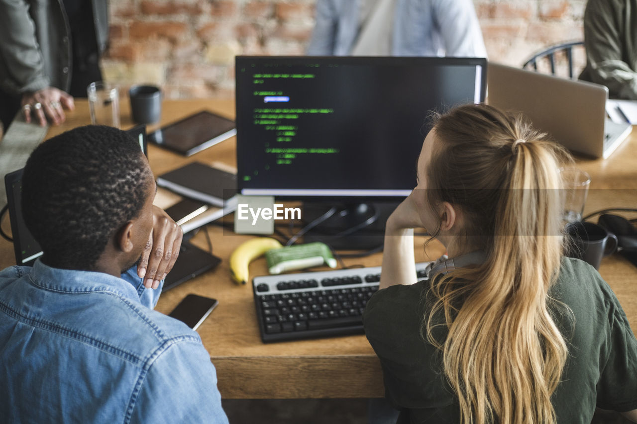 Rear view of male and female colleagues coding over computer at startup company