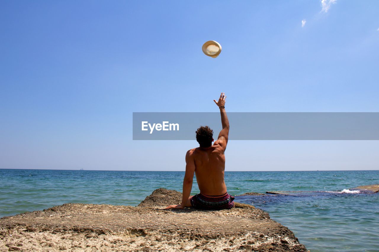 Rear view of shirtless man on beach against sky