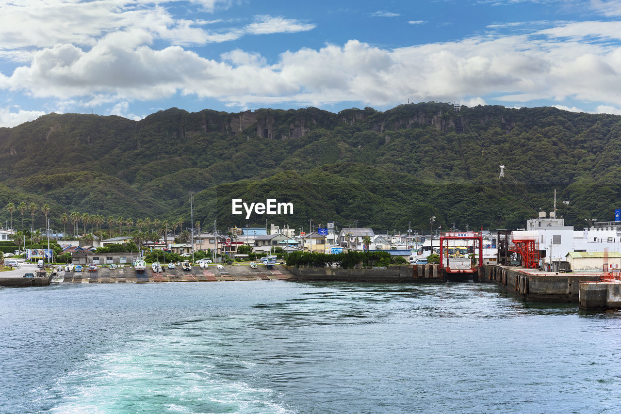 SCENIC VIEW OF SEA BY BUILDINGS AGAINST MOUNTAINS