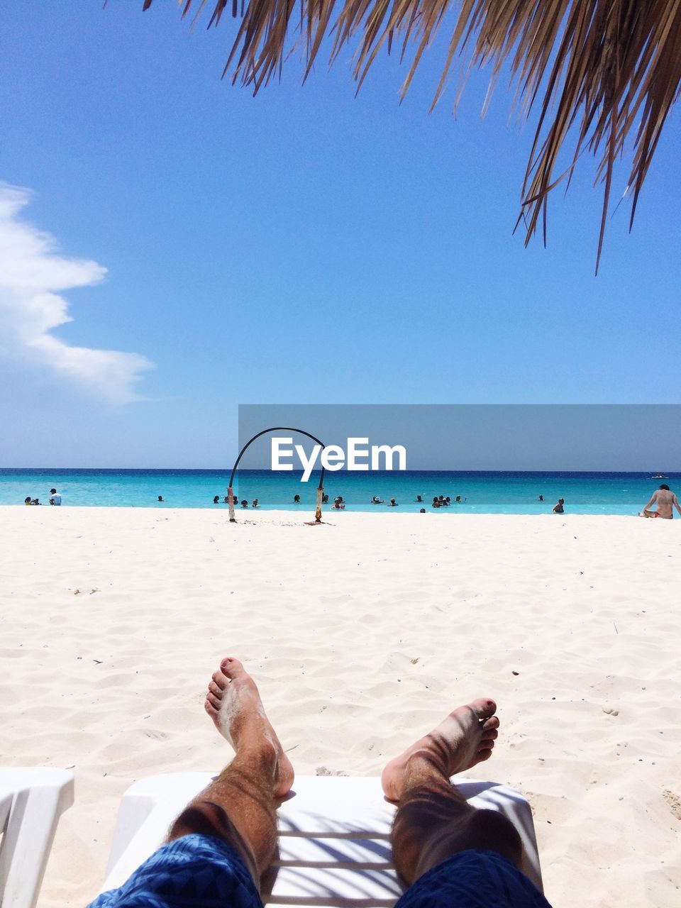 Low section of man relaxing at beach against blue sky during sunny day