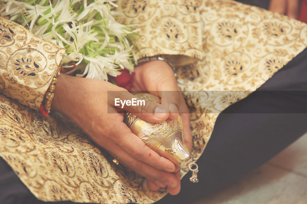 Midsection of groom with jewelry sitting on floor during wedding ceremony