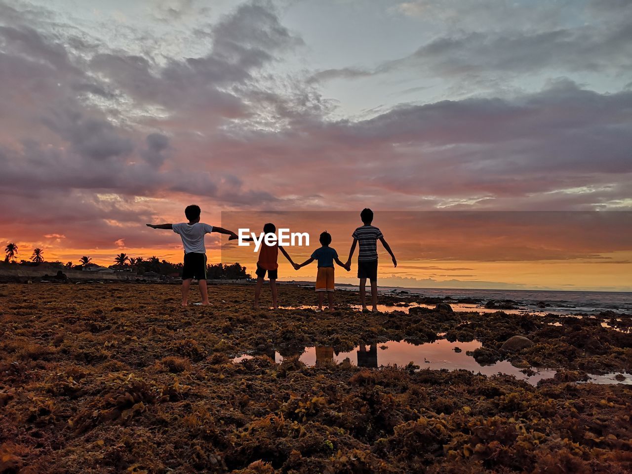 PEOPLE STANDING AT BEACH AGAINST SKY DURING SUNSET