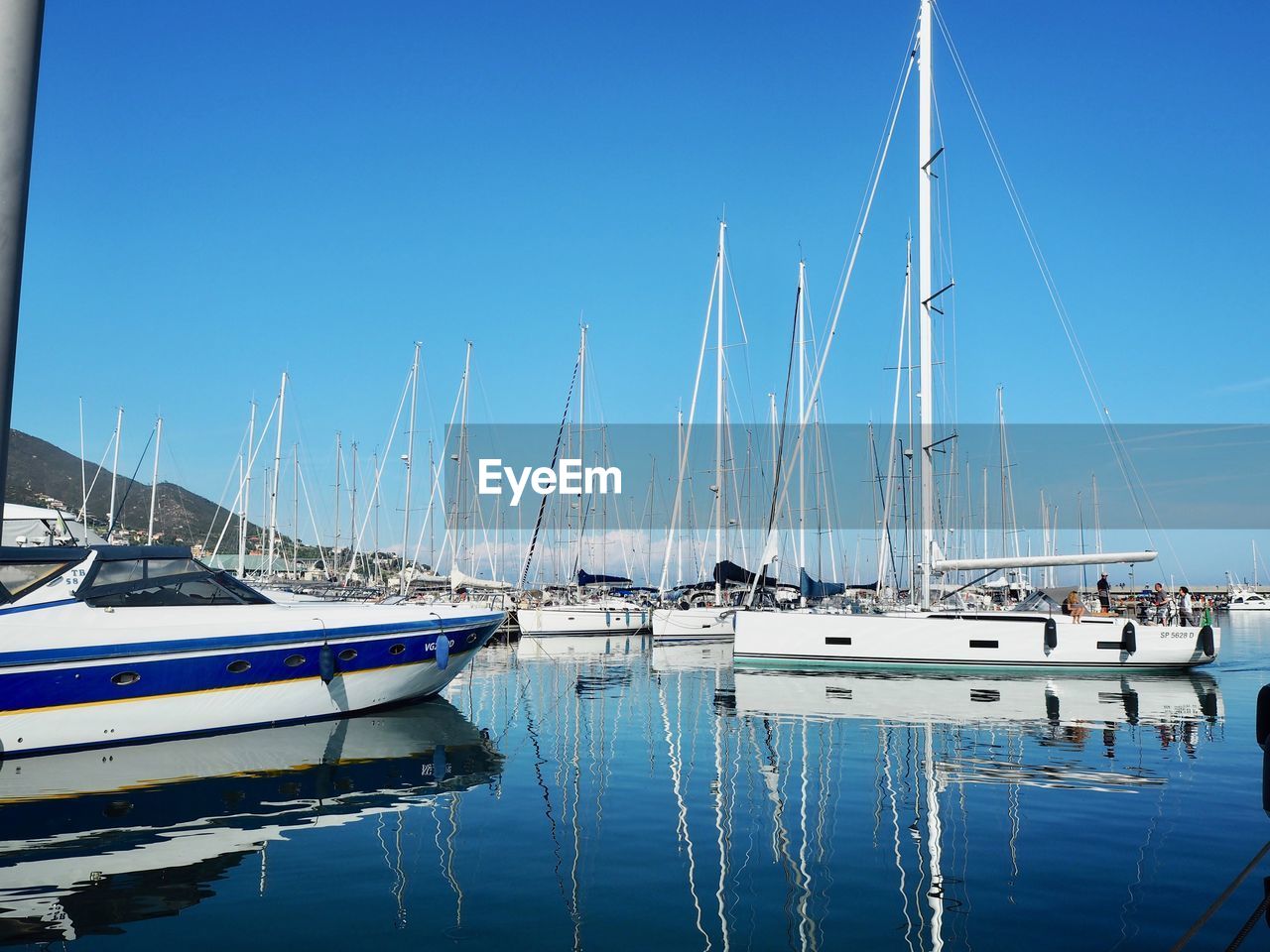 Sailboats moored at harbor against clear blue sky