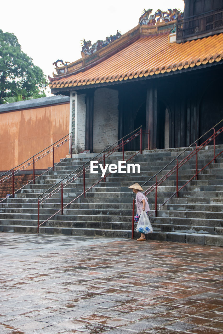 GIRL STANDING ON STAIRCASE AGAINST BUILDING