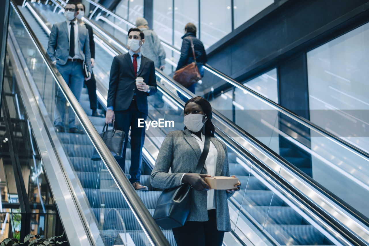 Male and female colleagues moving downwards on escalator during covid-19