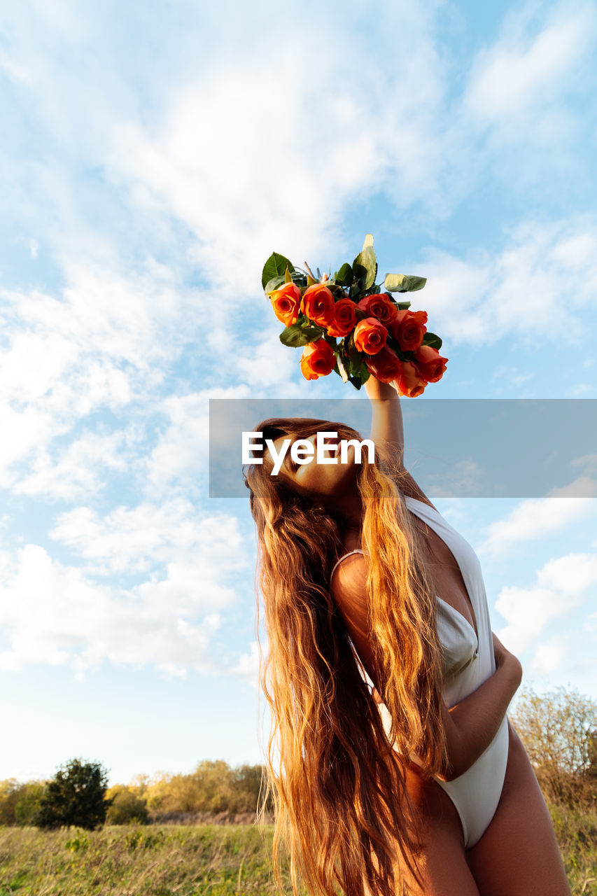 Woman standing by flowering plant against sky