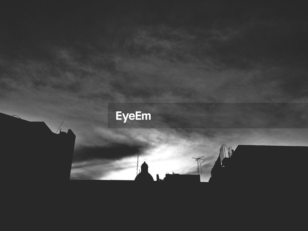 Low angle view of silhouette buildings against cloudy sky