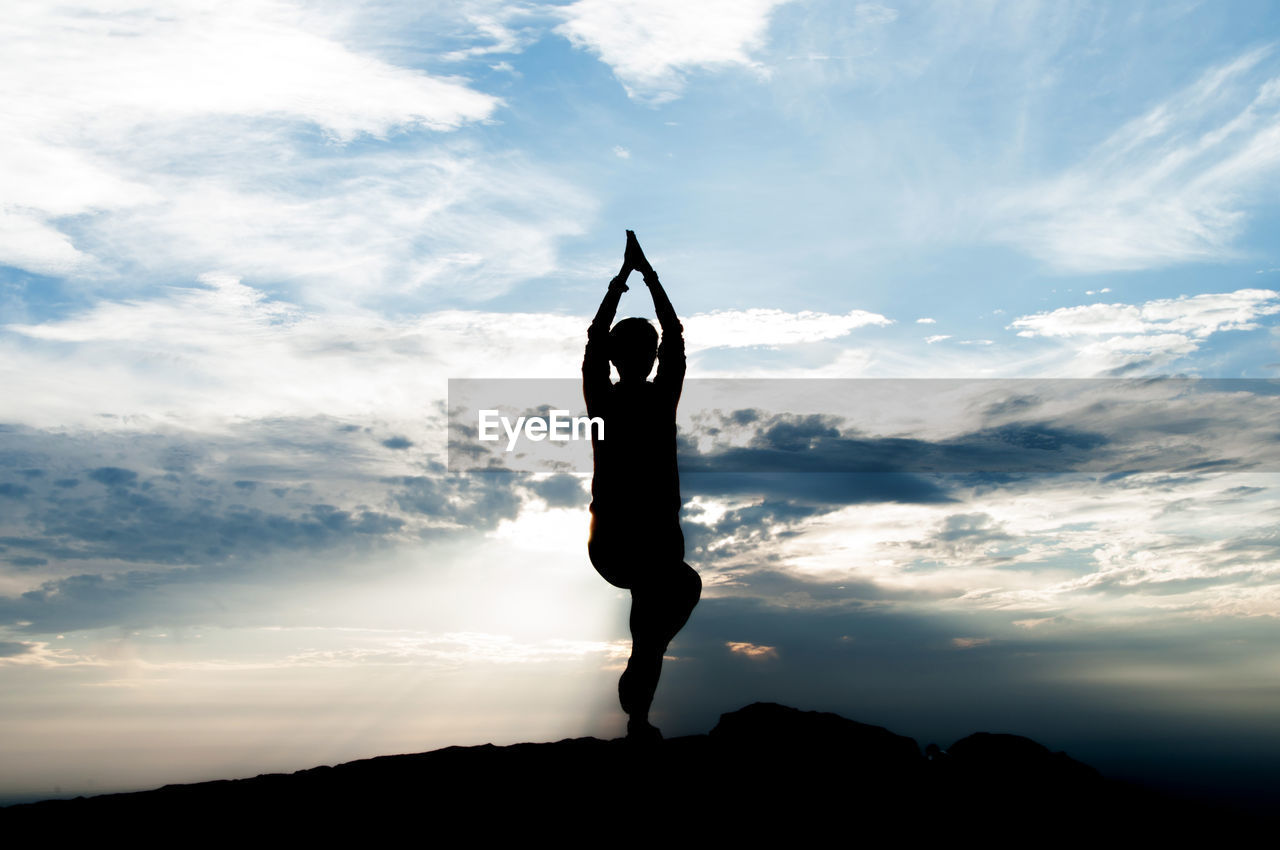 Silhouette person doing yoga against cloudy sky at dusk