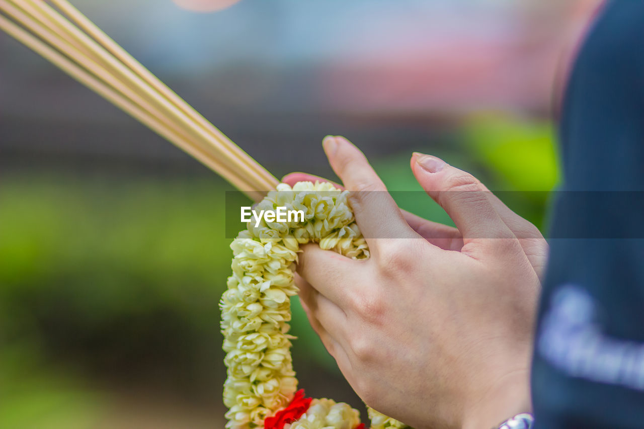 Cropped hands of woman holding incense sticks with floral garland in temple