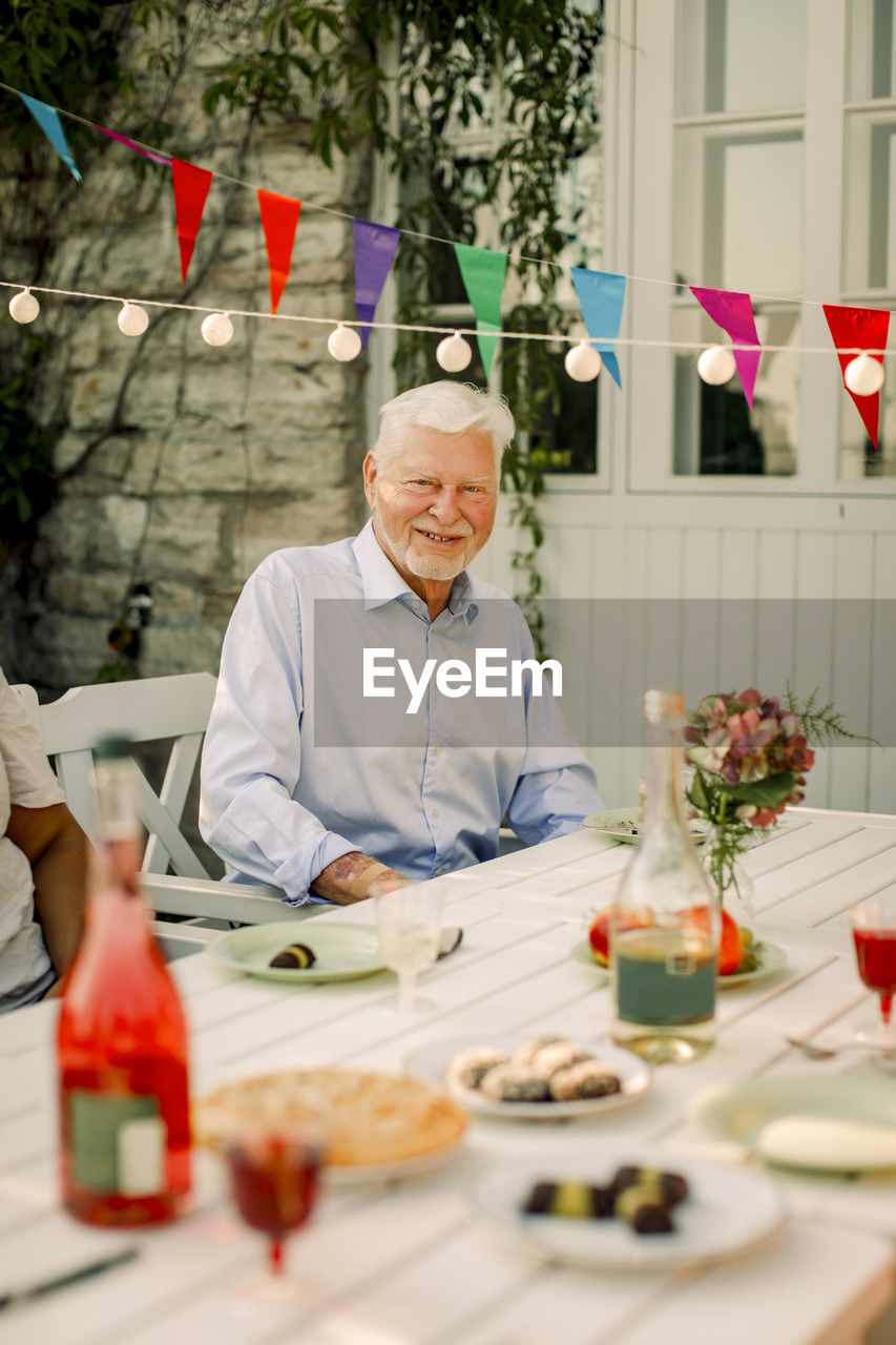 Portrait of smiling senior man sitting at dining table in back yard