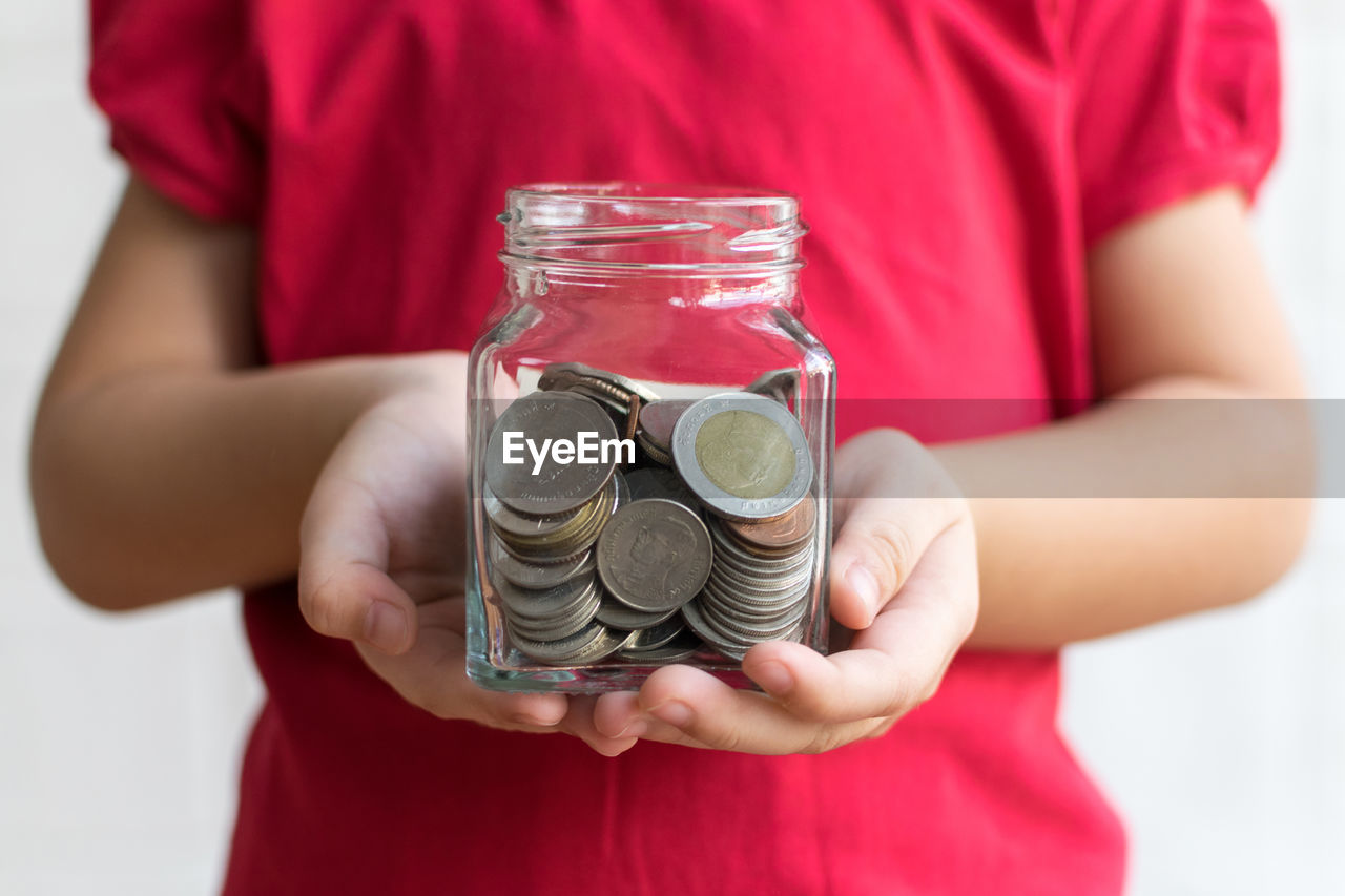 Midsection of boy holding coins in jar