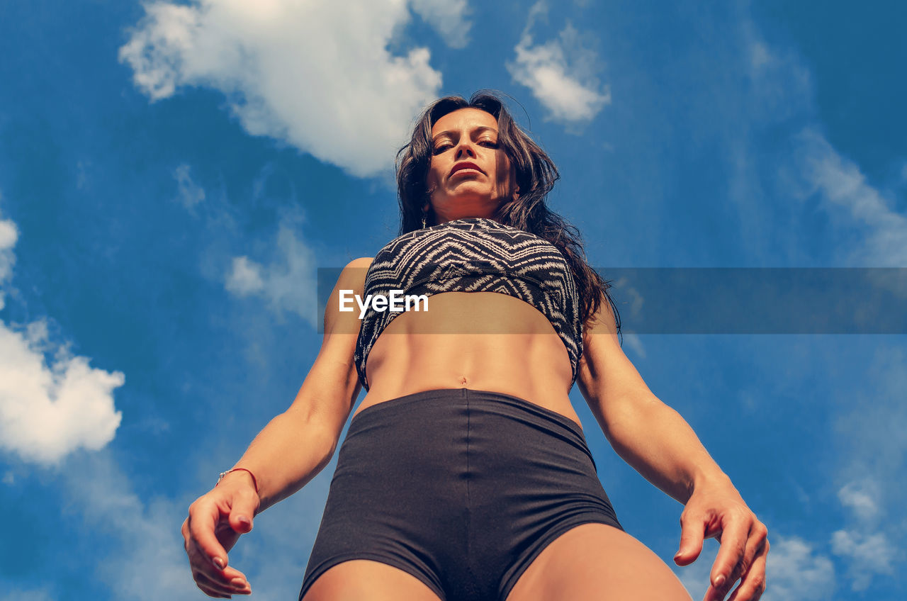 Fitness woman in shorts and top on a background of sky clouds