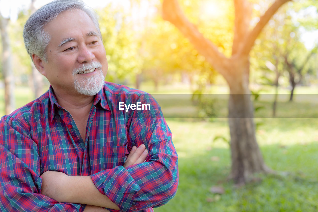 Thoughtful senior man with arms crossed at park