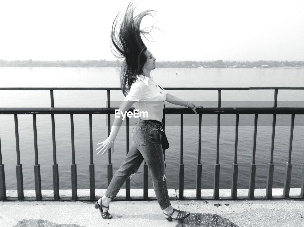 Side view of woman walking by railing on bridge with tousled hair