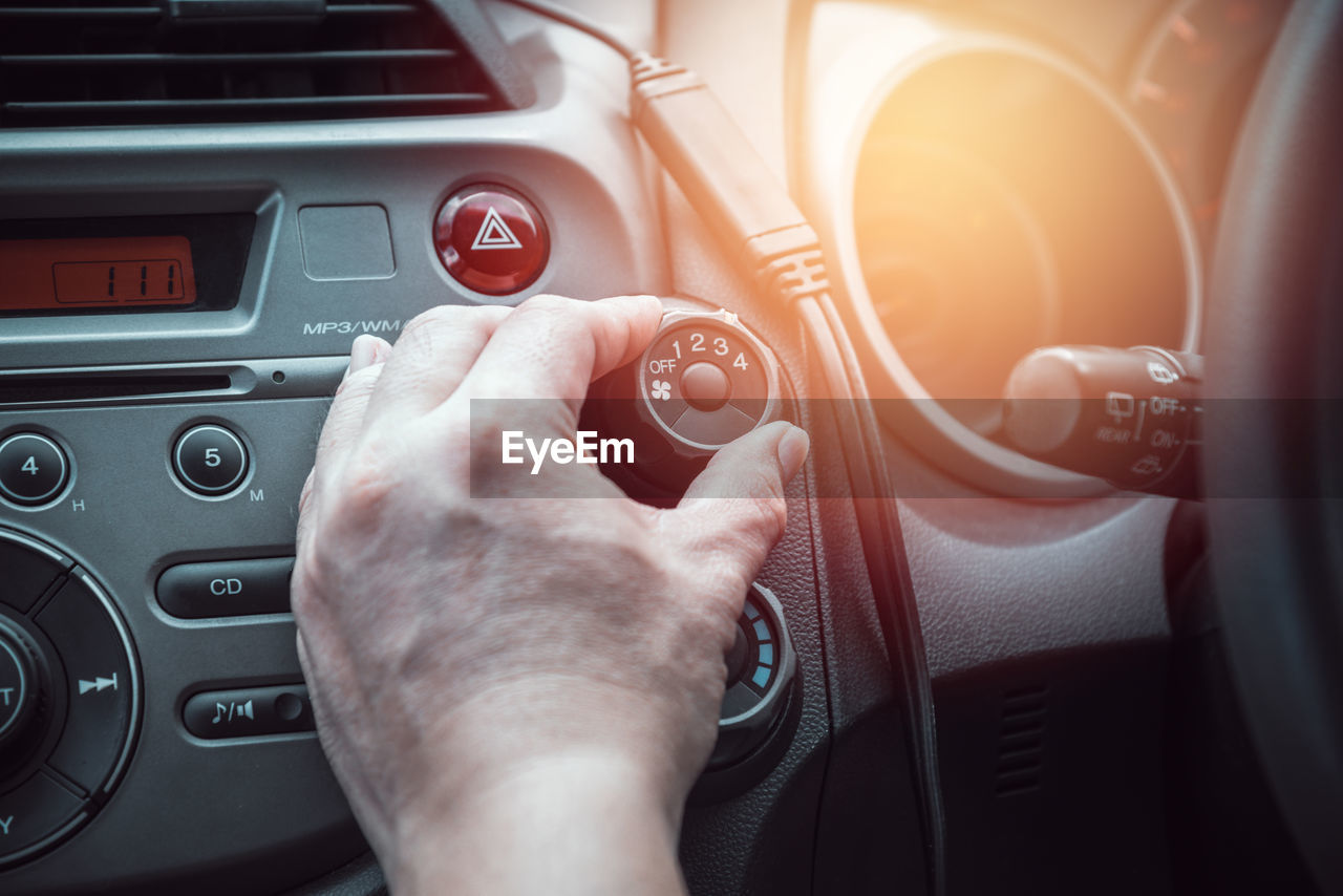 Cropped hand of man adjusting fan button in car