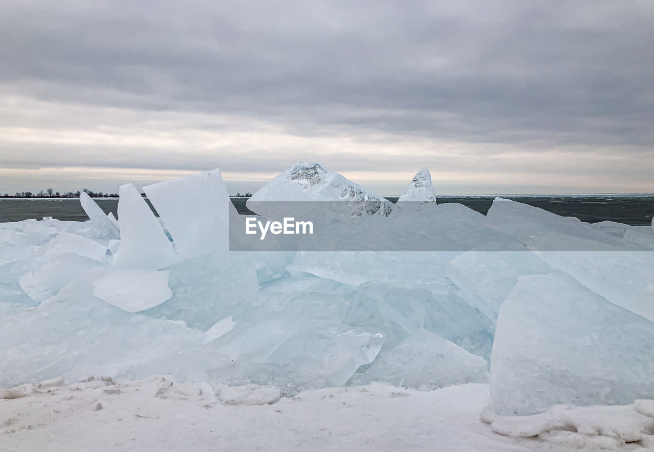 Large flat pieces of ice piled up along the shore of a lake in winter.