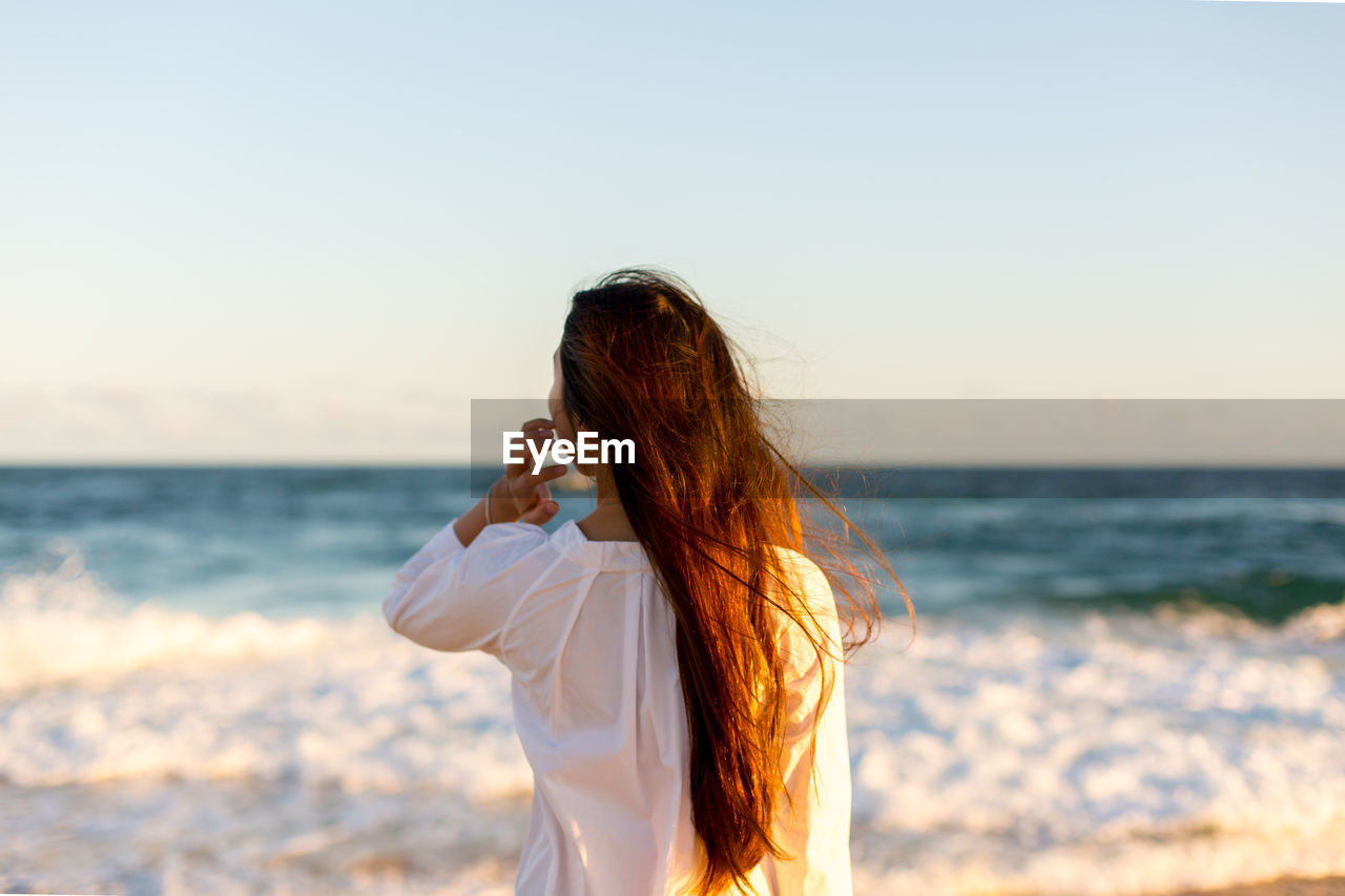 Rear view of woman standing at beach against clear sky