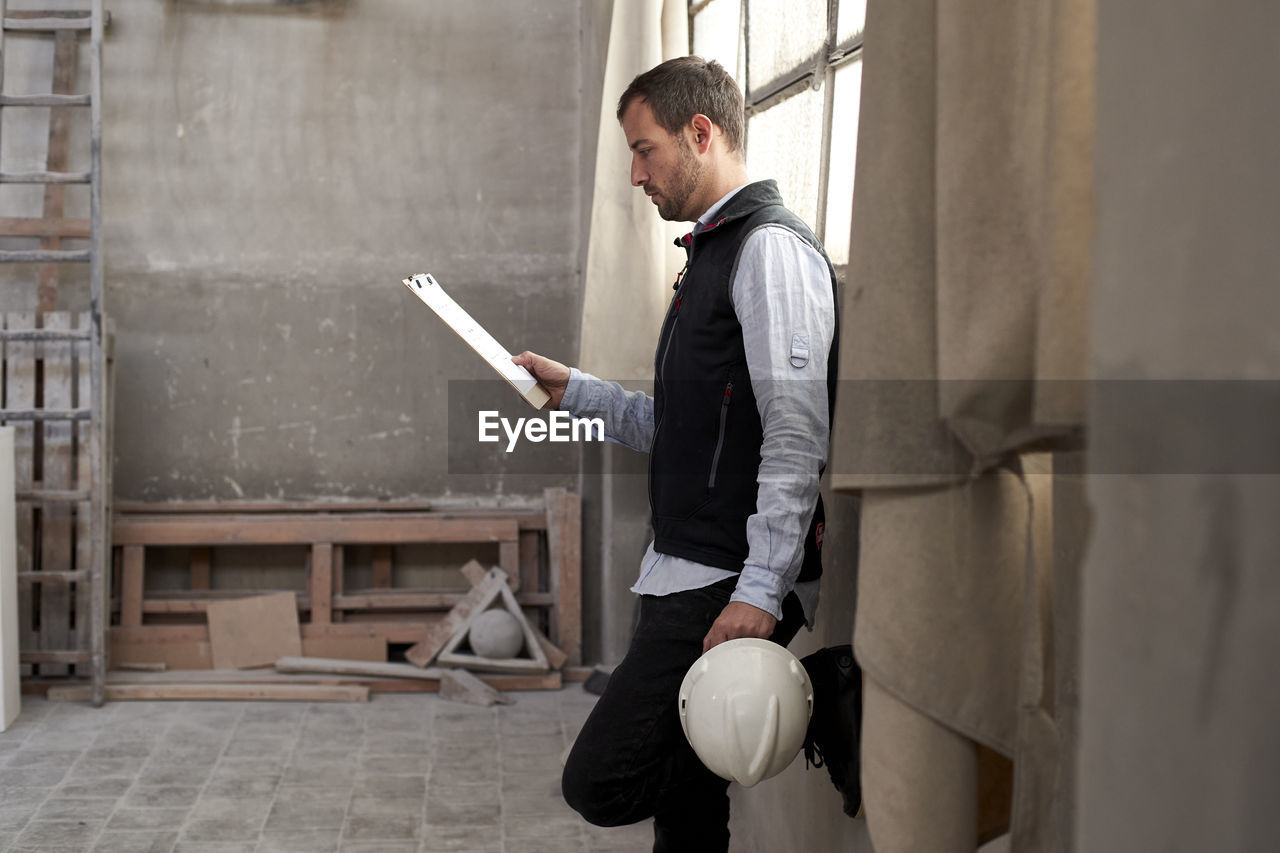 Male contractor analyzing document while standing in building