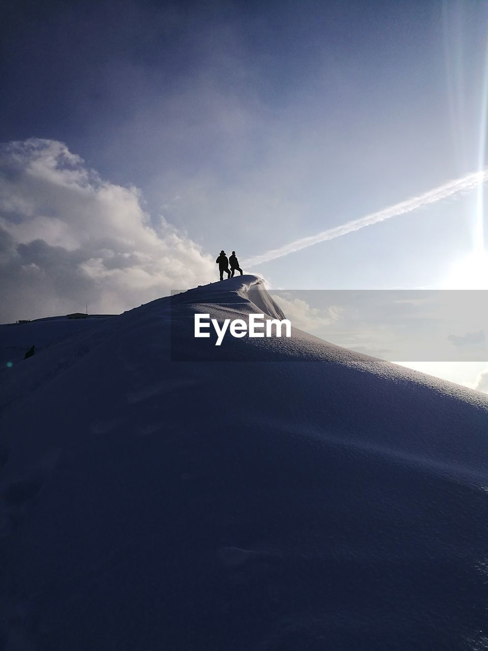 Low angle view of silhouette men standing on snowcapped mountain against sky