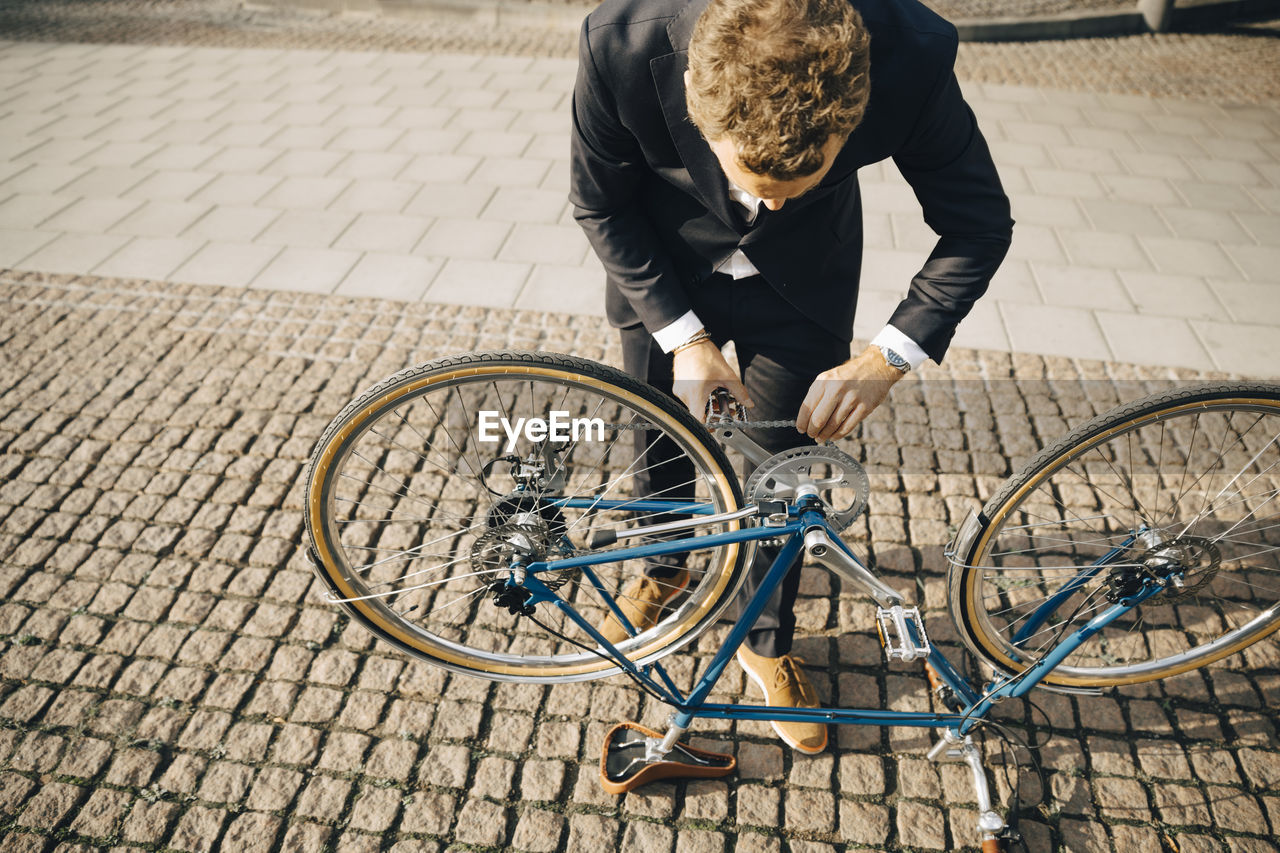 High angle view of businessman repairing bicycle chain on cobbled footpath in city