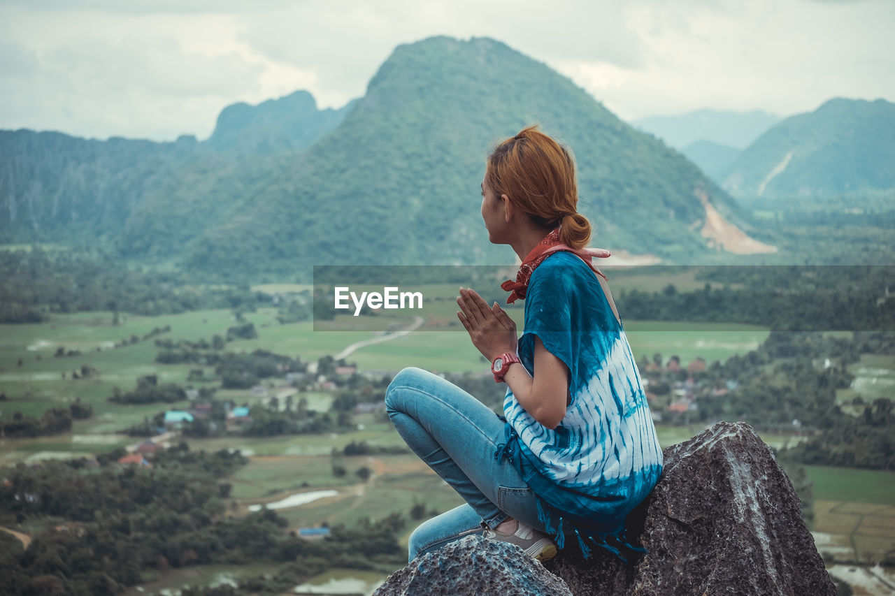 Side view of mid adult woman sitting on cliff against mountains