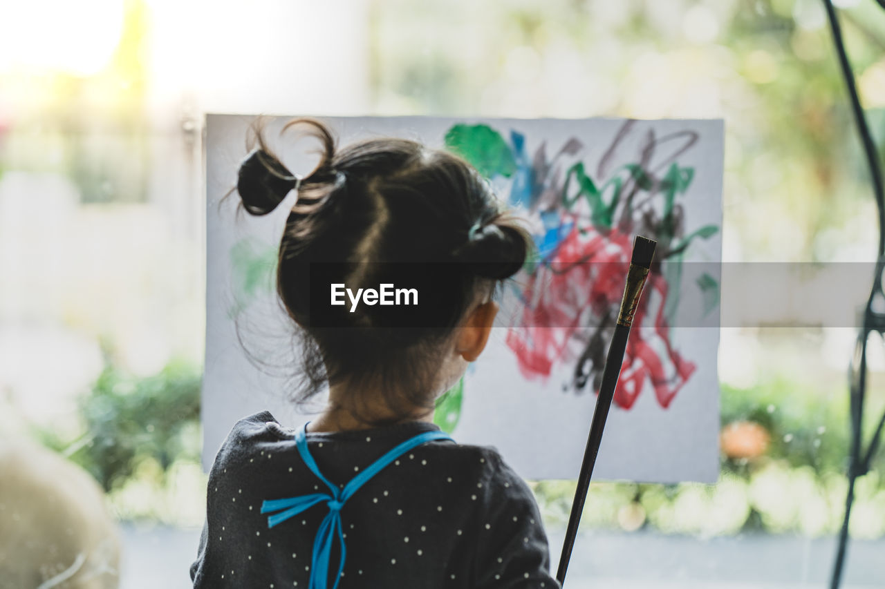 Rear view of girl painting on paper